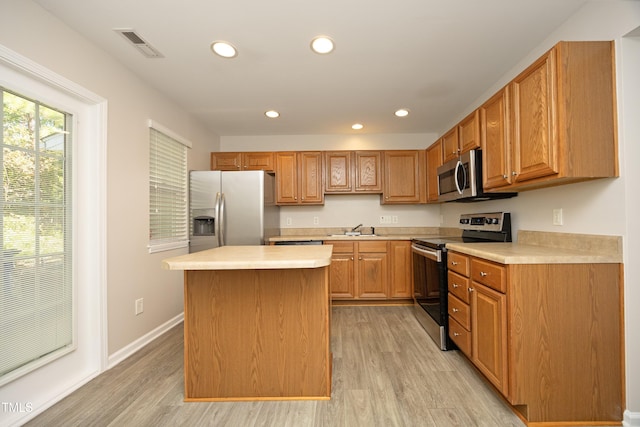 kitchen with stainless steel appliances, a center island, sink, and light hardwood / wood-style flooring