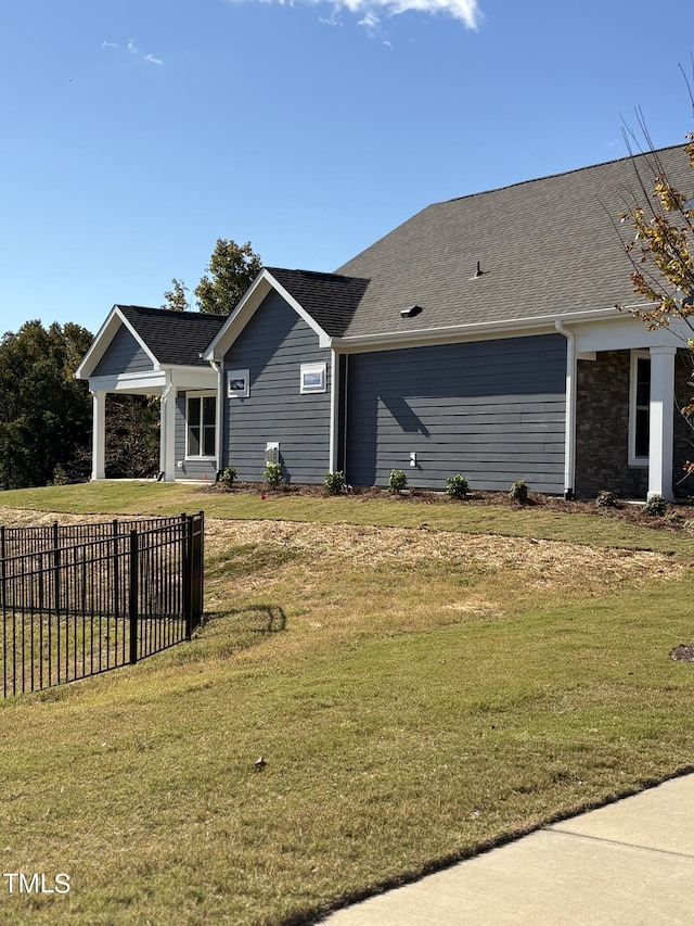 view of home's exterior featuring a lawn, fence, and a shingled roof
