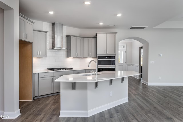 kitchen featuring a kitchen island with sink, sink, wall chimney range hood, gray cabinets, and dark hardwood / wood-style floors