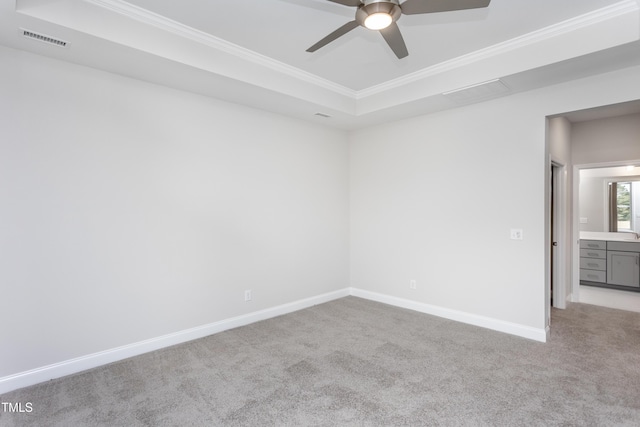 empty room with light colored carpet, a raised ceiling, ceiling fan, and crown molding