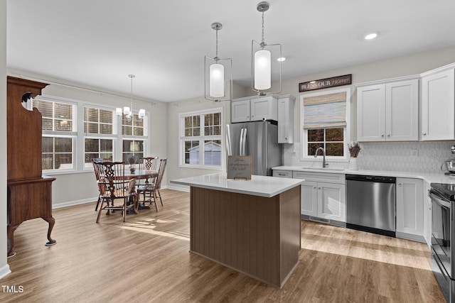 kitchen with white cabinetry, stainless steel appliances, hanging light fixtures, and a kitchen island