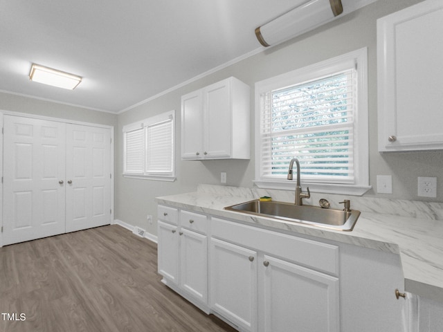 kitchen with ornamental molding, white cabinetry, sink, and light wood-type flooring