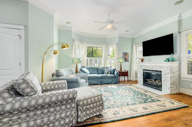 living room featuring crown molding, a stone fireplace, hardwood / wood-style flooring, and ceiling fan