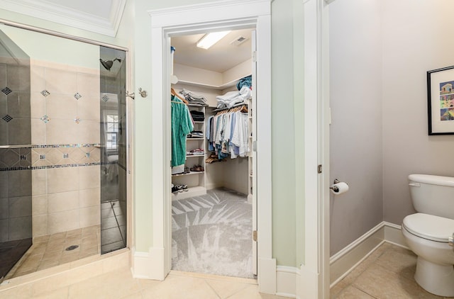 bathroom featuring tile patterned flooring, toilet, ornamental molding, and tiled shower