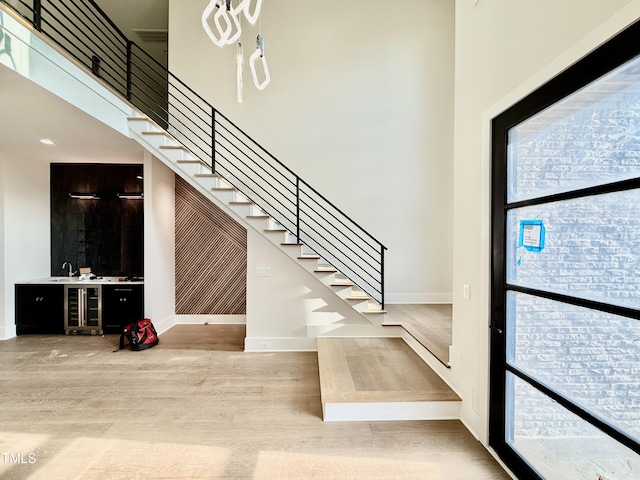 foyer with sink, a towering ceiling, light hardwood / wood-style flooring, and beverage cooler