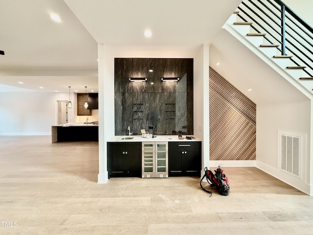 bar with wine cooler, light wood-type flooring, sink, and pendant lighting