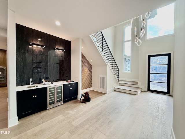 bar with wine cooler, sink, a high ceiling, and light wood-type flooring