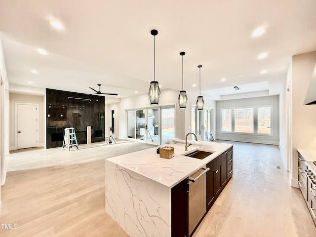 kitchen featuring sink, light stone counters, a center island with sink, dishwasher, and pendant lighting