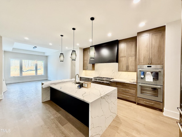 kitchen with appliances with stainless steel finishes, pendant lighting, light stone countertops, custom range hood, and a center island with sink