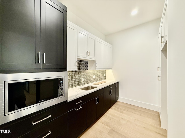 kitchen featuring built in microwave, sink, white cabinetry, light hardwood / wood-style floors, and backsplash