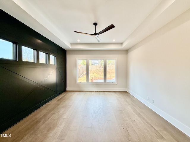 spare room featuring a raised ceiling, ceiling fan, and light wood-type flooring