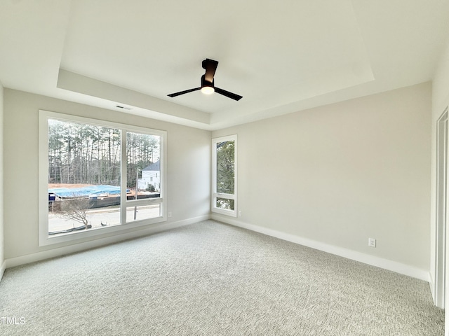 carpeted spare room featuring ceiling fan and a raised ceiling