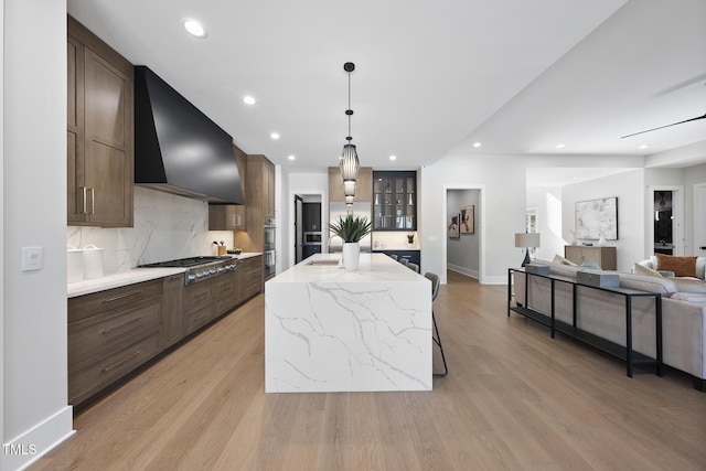 kitchen featuring tasteful backsplash, recessed lighting, light wood-style flooring, appliances with stainless steel finishes, and wall chimney exhaust hood