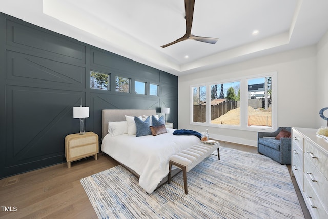 bedroom with a tray ceiling, ceiling fan, light wood-style flooring, and recessed lighting