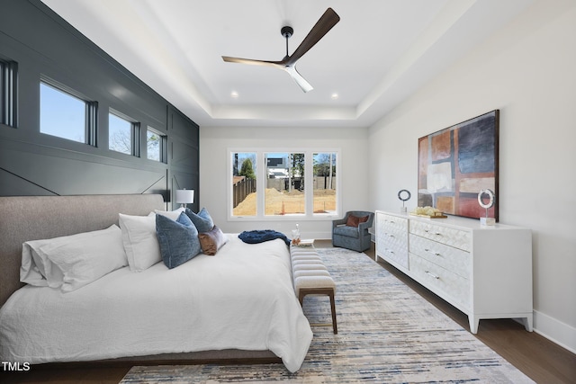 bedroom with recessed lighting, a raised ceiling, a ceiling fan, wood finished floors, and baseboards