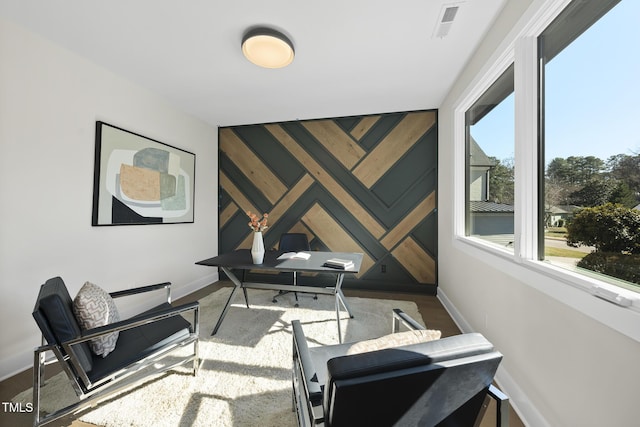 office area with an accent wall, visible vents, baseboards, and wood finished floors