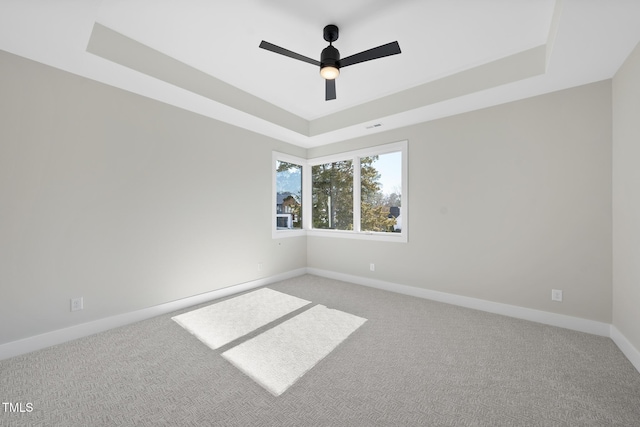 spare room featuring a ceiling fan, a raised ceiling, light carpet, and baseboards