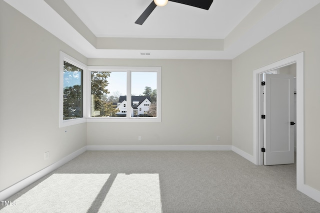 spare room featuring a raised ceiling, light colored carpet, visible vents, and baseboards