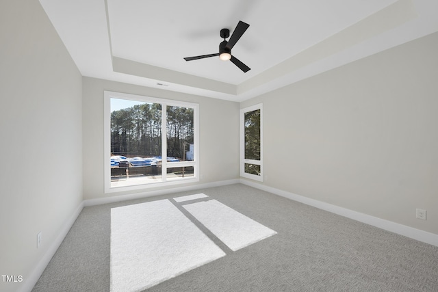 empty room with a tray ceiling, carpet flooring, a ceiling fan, and baseboards