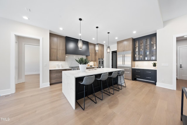 kitchen featuring a kitchen bar, backsplash, light wood-style floors, an island with sink, and baseboards