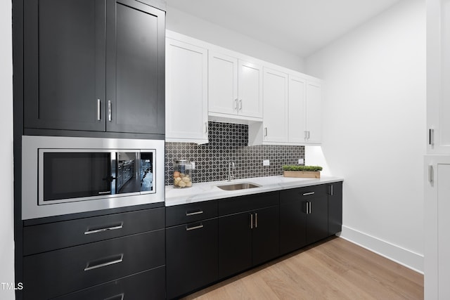 kitchen featuring decorative backsplash, white cabinets, a sink, built in microwave, and dark cabinetry