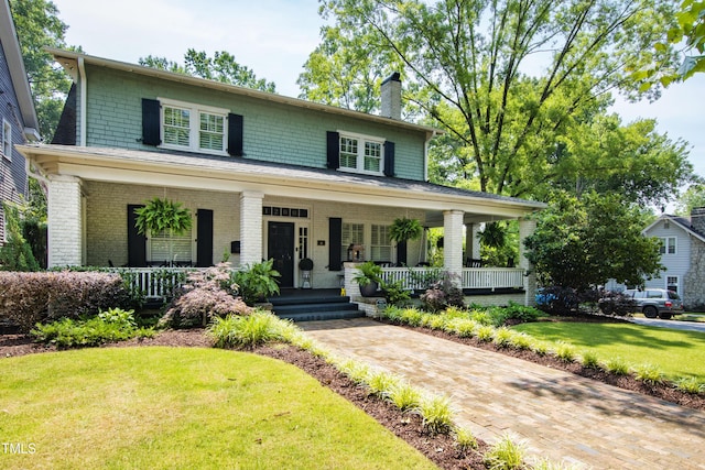 view of front facade with covered porch, brick siding, a chimney, and a front lawn