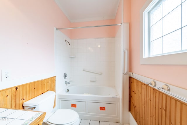 bathroom with tile patterned flooring, toilet, tiled shower / bath combo, and wooden walls