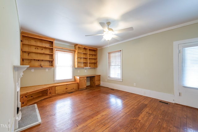 unfurnished office featuring built in desk, ceiling fan, wood-type flooring, and ornamental molding