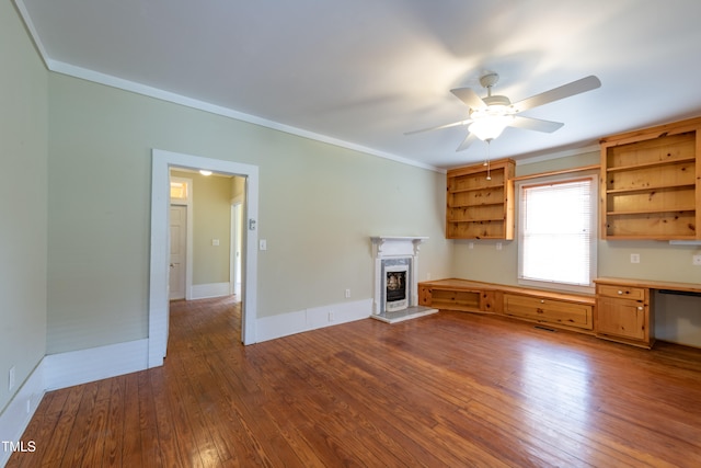 unfurnished living room with built in desk, ceiling fan, crown molding, and wood-type flooring