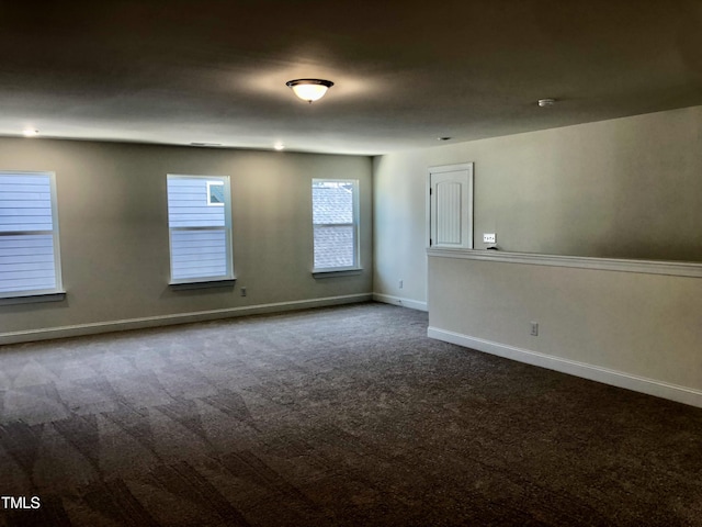 spare room featuring dark carpet and baseboards