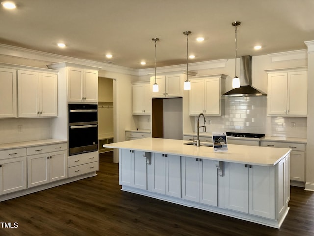 kitchen featuring an island with sink, wall chimney range hood, white cabinetry, and a sink