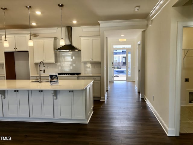 kitchen with dark wood-style floors, decorative backsplash, ornamental molding, a sink, and wall chimney range hood