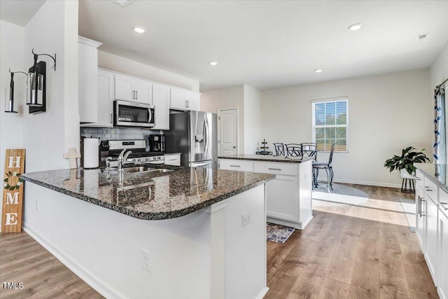 kitchen featuring white cabinetry, a kitchen island with sink, stainless steel appliances, and light wood-type flooring