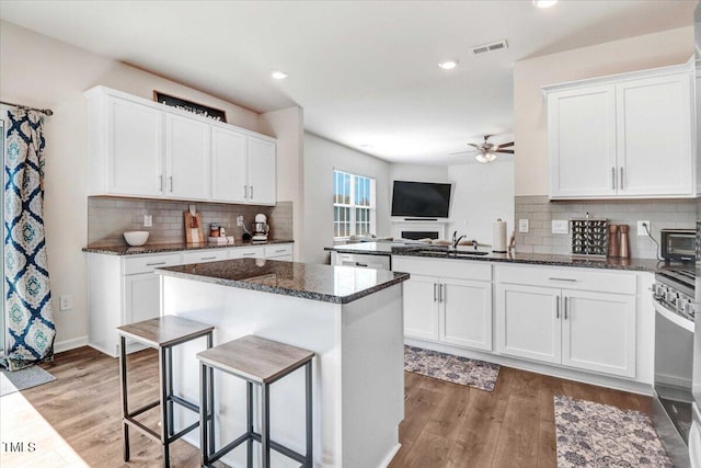 kitchen with white cabinets, hardwood / wood-style floors, a kitchen island, black stove, and dark stone countertops