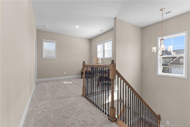 hall with carpet flooring, an inviting chandelier, an upstairs landing, visible vents, and baseboards