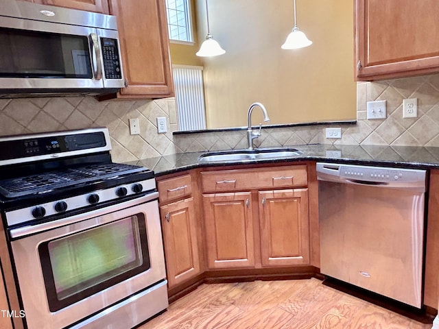 kitchen with dark stone countertops, stainless steel appliances, sink, and hanging light fixtures