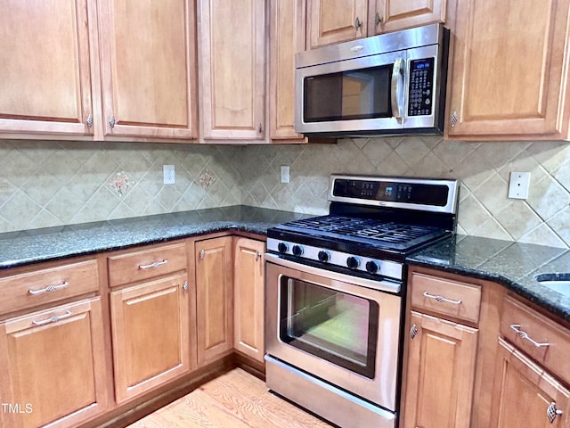 kitchen with stainless steel appliances, tasteful backsplash, dark stone counters, and light wood-type flooring