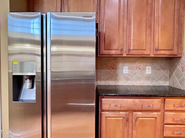 kitchen featuring dark stone countertops, tasteful backsplash, and stainless steel fridge