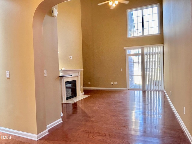 unfurnished living room with a premium fireplace, ceiling fan, wood-type flooring, and a towering ceiling