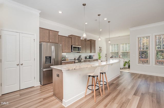 kitchen featuring a kitchen island with sink, hanging light fixtures, crown molding, appliances with stainless steel finishes, and light hardwood / wood-style floors