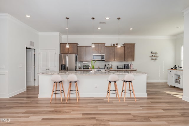 kitchen with a kitchen island with sink, stainless steel appliances, a kitchen bar, and pendant lighting