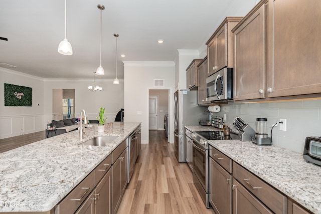 kitchen featuring a center island with sink, light hardwood / wood-style flooring, sink, pendant lighting, and stainless steel appliances