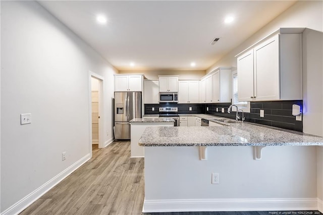 kitchen featuring a kitchen breakfast bar, light hardwood / wood-style flooring, kitchen peninsula, white cabinetry, and appliances with stainless steel finishes