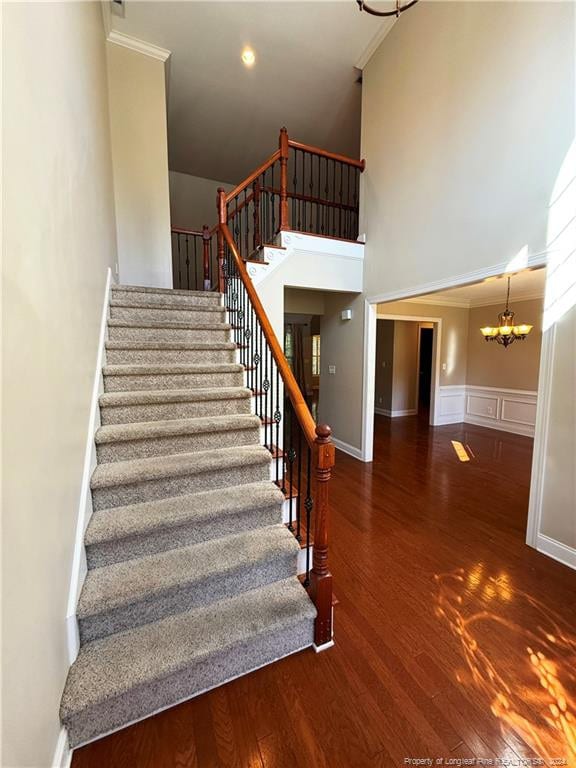 staircase featuring wood-type flooring, crown molding, and an inviting chandelier