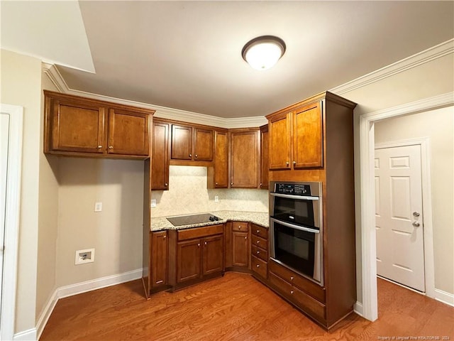 kitchen with light stone countertops, black electric stovetop, double oven, crown molding, and hardwood / wood-style flooring