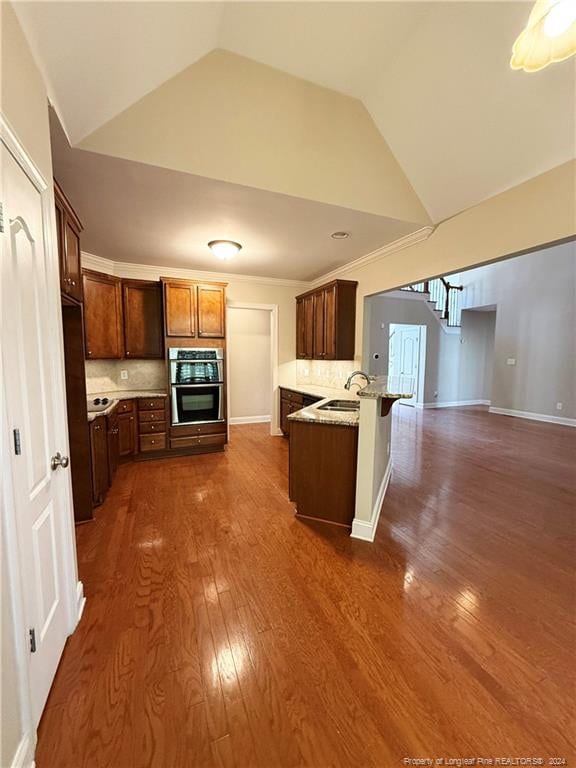 kitchen with vaulted ceiling, decorative backsplash, double oven, and dark hardwood / wood-style floors