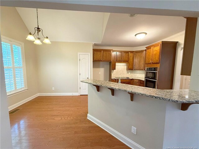 kitchen featuring hanging light fixtures, a notable chandelier, double oven, light hardwood / wood-style floors, and a breakfast bar area