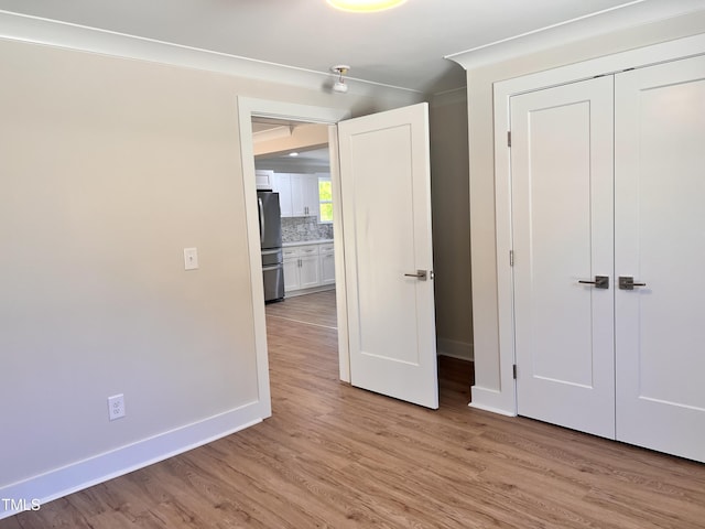 unfurnished bedroom featuring baseboards, freestanding refrigerator, a closet, and light wood-style flooring