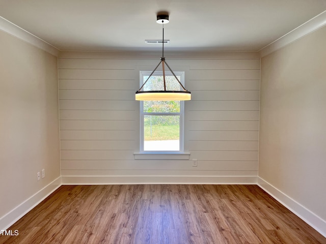 unfurnished dining area with visible vents, baseboards, crown molding, and wood finished floors