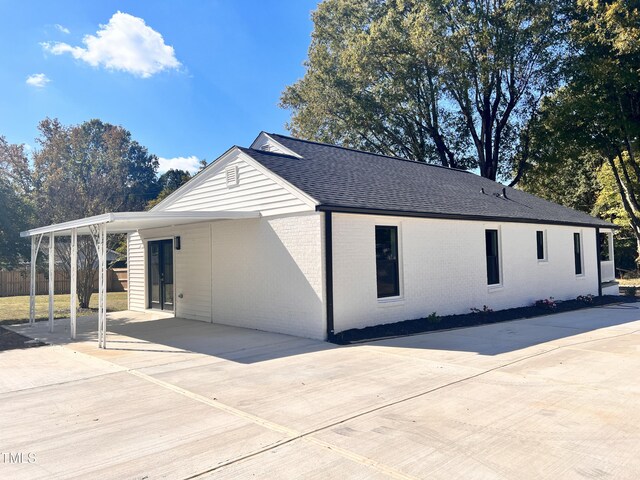 view of home's exterior featuring fence, an attached carport, brick siding, a shingled roof, and driveway